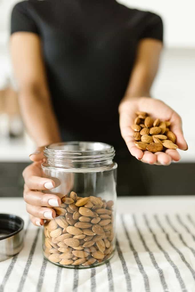 A person pours almonds from hand into a glass jar, ready for a healthy snack.