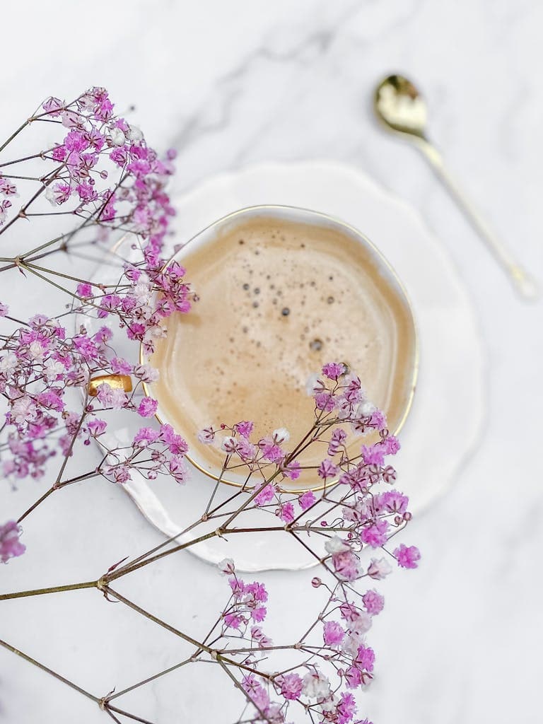 A stylish coffee cup surrounded by pink gypsophila on a marble surface, creating an ethereal and pastel aesthetic.