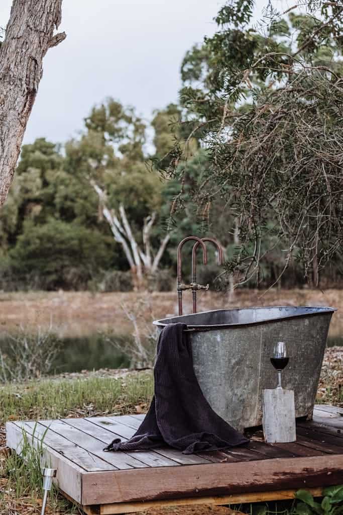 An outdoor rustic bath setup by a tranquil lake, surrounded by lush greenery and natural beauty.