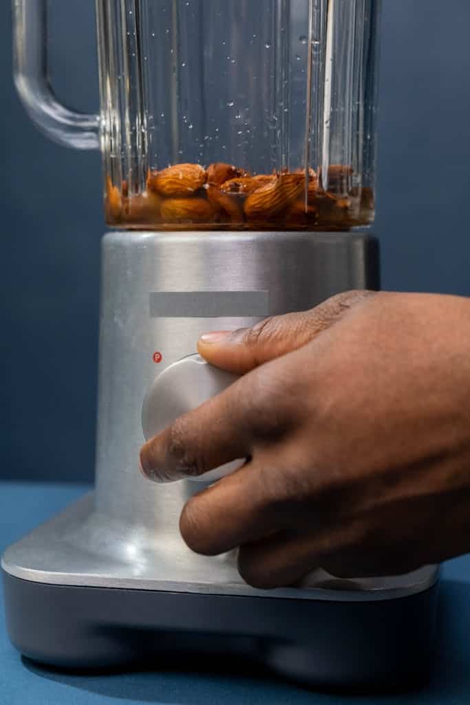 Detailed image of a hand turning on a blender with almonds inside. Ideal for kitchen and appliance themes.