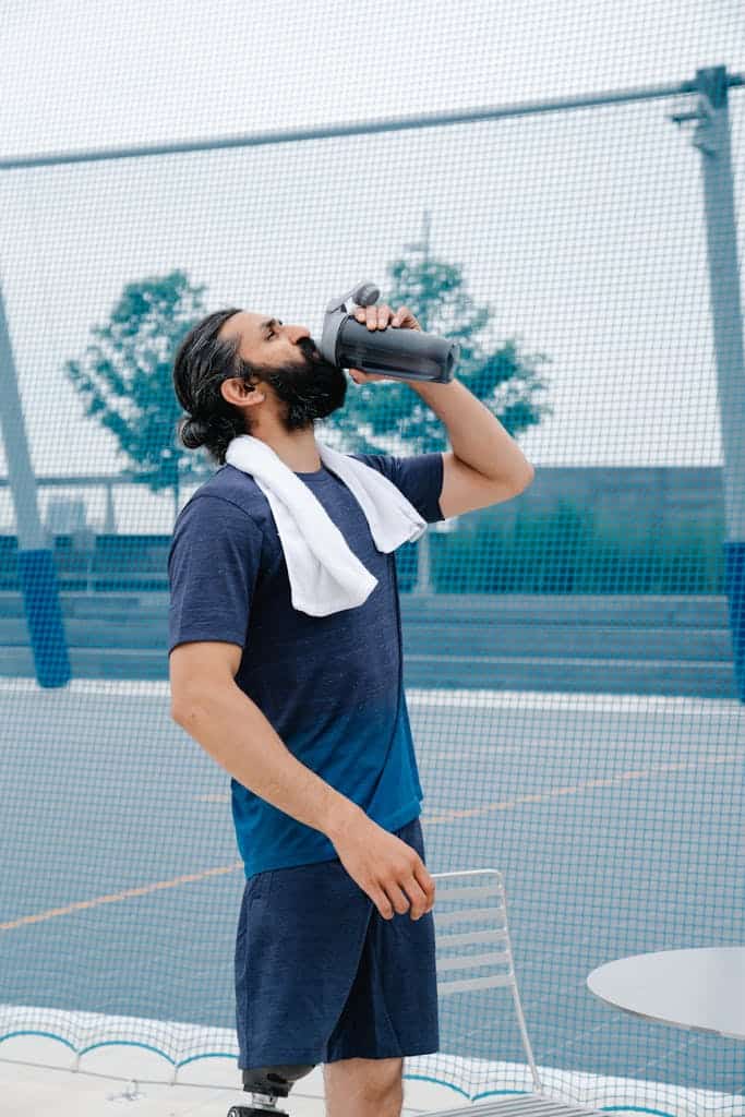 Man in sportswear drinking water outdoors after exercising, promoting fitness and hydration.