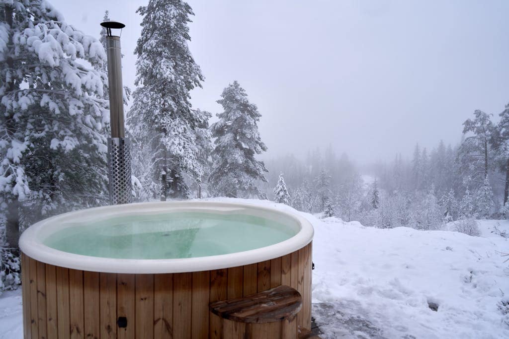 Relaxing hot tub amidst snow-covered trees in a serene Norwegian winter landscape.