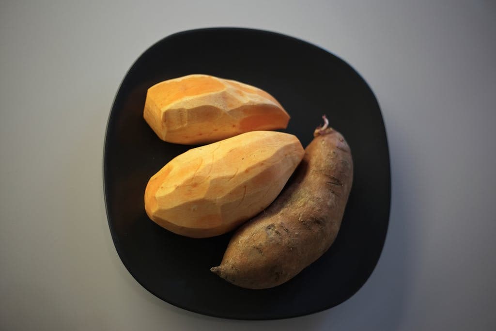 Three sweet potatoes on a black plate, showcasing fresh and rustic appeal.