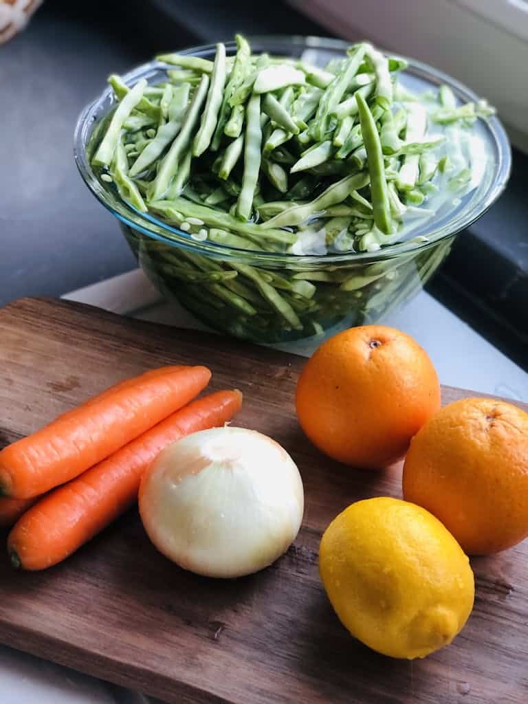 Vibrant fresh vegetables and fruits arranged on a wooden cutting board by the window.