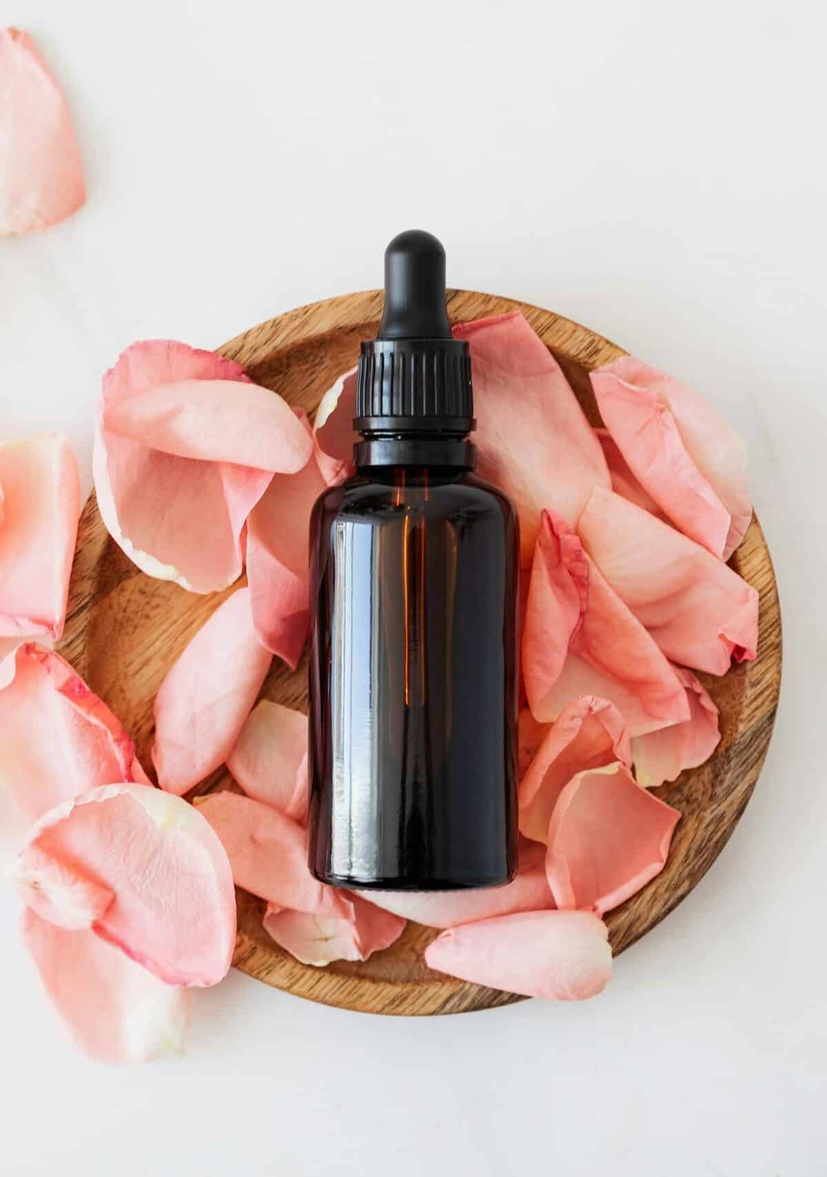 Nutrition Top view of empty brown bottle for skin care product placed on wooden plate with fresh pink rose petals on white background isolated