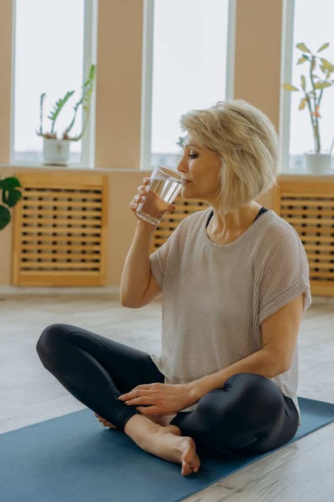massage therapist woman drinking water while seated on an exercise mat for self-care and proper hydration.
