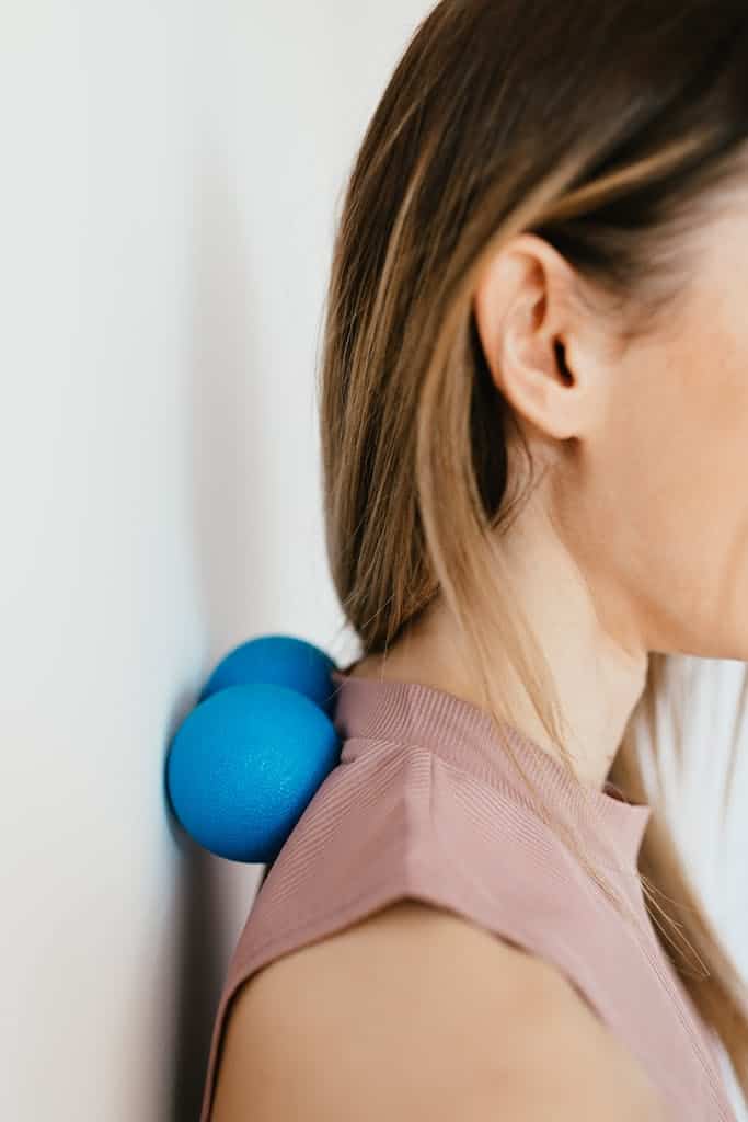 massage therapist using blue massage balls against a wall for neck and shoulder tension relief for self care and to improve energy